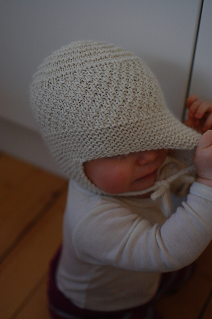 Baby- eller barnelue med øreklaffer og snor med pomponger
